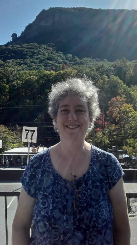A picture of Lara at Chimney Rock, North Carolina. In front of trees and there is a small sign with the number 77 on it
